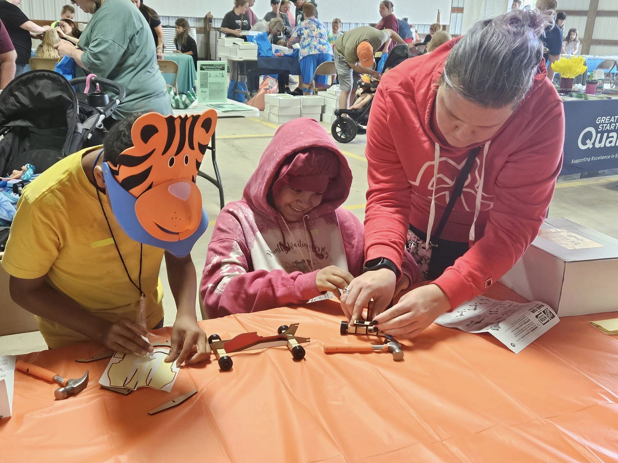 Two children making a craft with a volunteer from Home Depot at the 2023 Touch A Truck